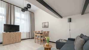 Ett modernt vardagsrum med en tv, ett träskåp, ett matbord, stolar, en soffa och ett litet runt bord med en vas.