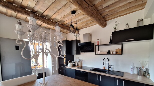 Een moderne keuken met donkere kastjes, een houten plafond, een kroonluchter en een flatscreen televisie.
