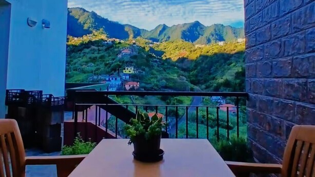A balcony with a table and chairs, overlooking a mountainous landscape with houses.