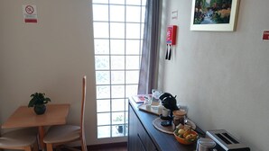 A small kitchenette with a table, chairs, a plant, a window with curtains, a painting, and a toaster.