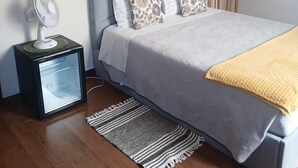 A bedroom with a bed, a nightstand with a fan, a lamp, a decorative wall piece, and a rug.