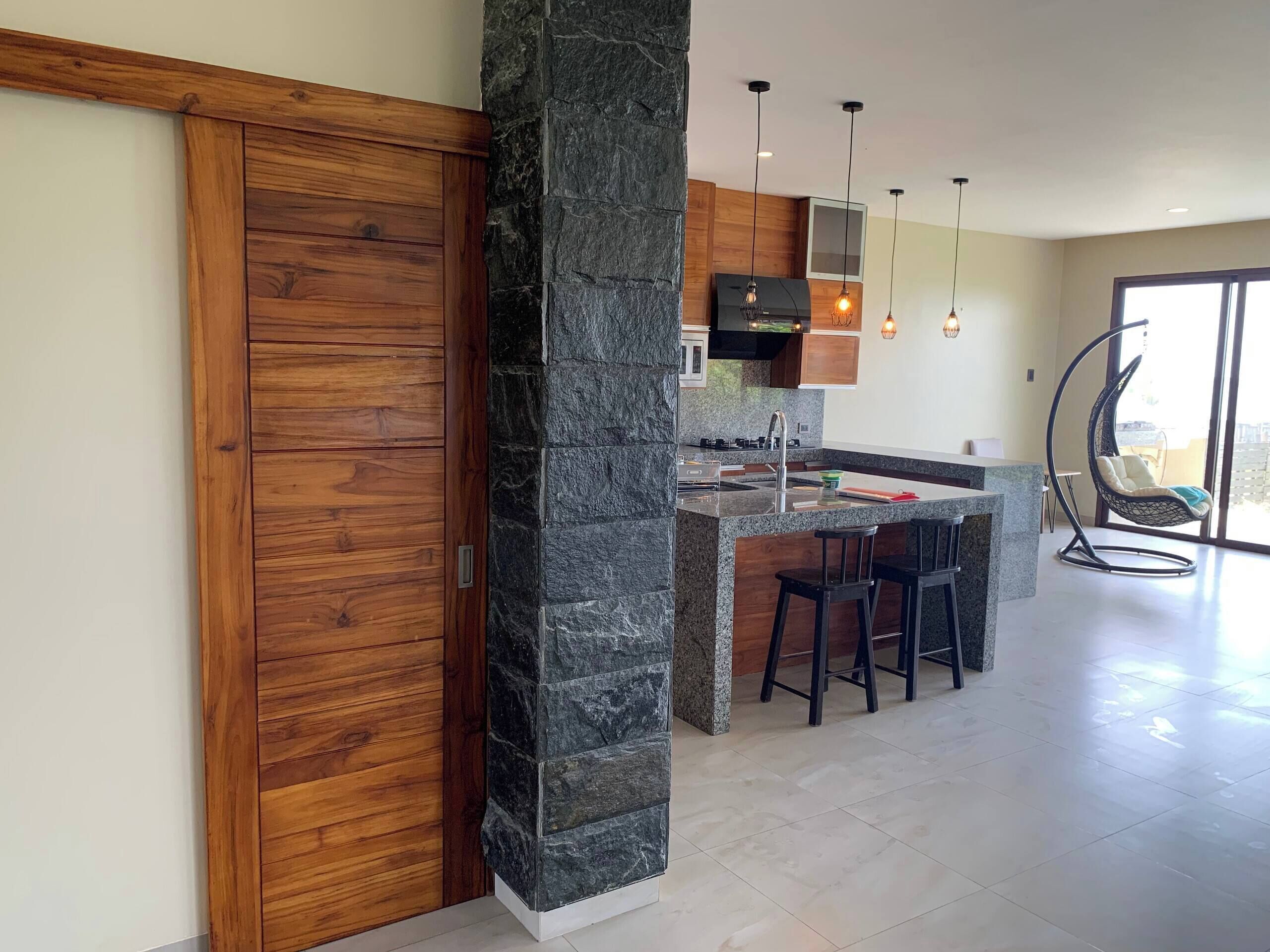 Une cuisine moderne avec une colonne en pierre, des armoires en bois et un fauteuil suspendu.