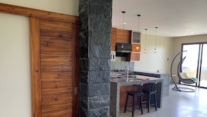 A modern kitchen with a stone column, wooden cabinets, and a hanging chair.