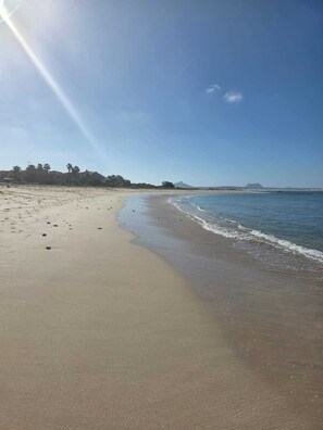 Ein Strand mit blauem Himmel, ruhiger See und fernen Bergen.