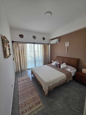 Ein Schlafzimmer mit einem Bett, Vorhängen, einem gemusterten Teppich, einer Wand-Klimaanlage und Wandbildern.