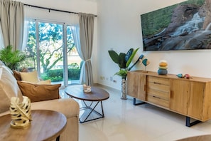 A modern living room with a sofa, a round coffee table, a wooden cabinet, and a large window with curtains. - Luxury Pool Condo Near Beach & Downtown (Punta Cana)