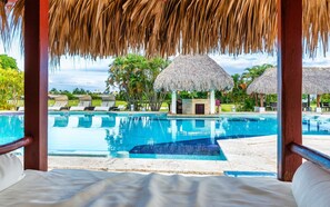 A pool area with lounge chairs and thatched umbrellas. - Luxury Pool Condo Near Beach & Downtown (Punta Cana)