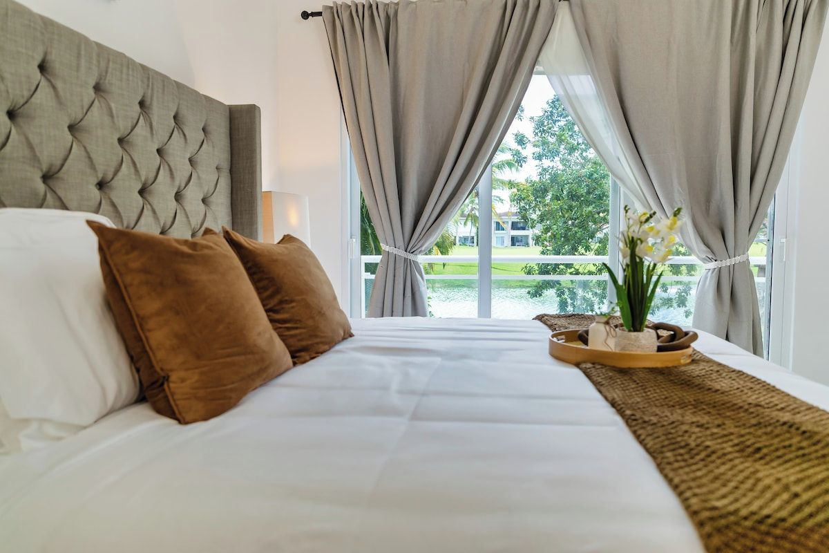 Ein Hotelzimmer mit einem großen Bett, einer gepolsterten Kopfstütze und Blick auf eine grüne Landschaft durch das Fenster.