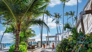 Ein Hotel direkt am Strand mit überdachter Sitzecke, Palmen und Meerblick.