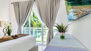 Ein Schlafzimmer mit Bett, Vorhängen, einem Fenster mit Blick auf einen Fluss und einem Nachttisch mit Pflanze.