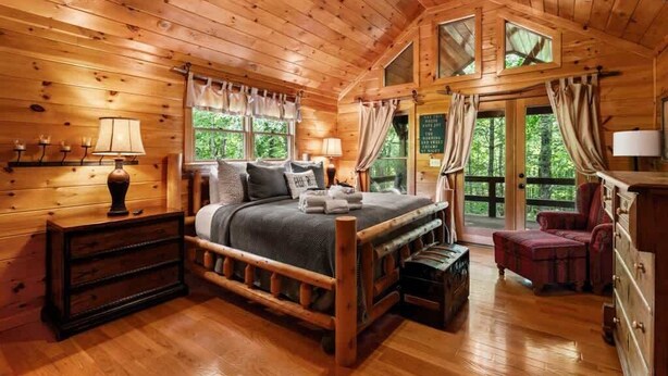 Een slaapkamer in een houten chalet met een bed, nachtkastjes, een dressoir en een raam met gordijnen.