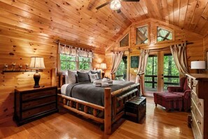 Une chambre dans une cabane en bois, avec un lit, des tables de chevet, une commode et une fenêtre avec des rideaux.