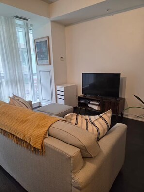 A living room with a sofa, a television, and a window with curtains. - Cozy 1-bedroom apartment with AC steps to attractions in downtown Toronto (Toronto)