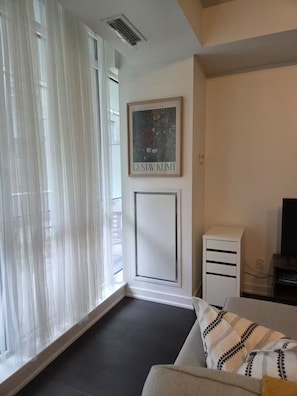 Olohuoneessa on sohva, kehystetty taideteos, valkoinen kaappi ja televisio.