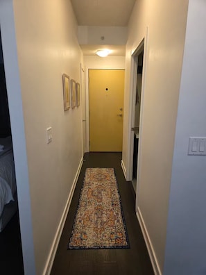 A narrow hallway with a patterned rug, a door at the end, and framed pictures on the wall. - Cozy 1-bedroom apartment with AC steps to attractions in downtown Toronto (Toronto)