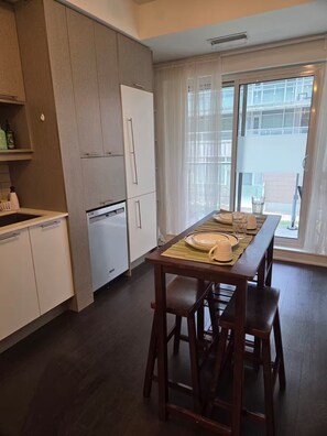 A modern kitchen with a dining area, including a table set for two with chairs, a refrigerator, and a window with curtains. - Cozy 1-bedroom apartment with AC steps to attractions in downtown Toronto (Toronto)