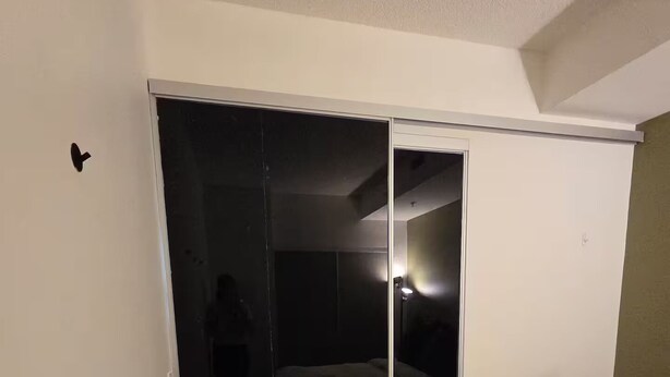 Ett hotellrum med en säng, en garderob med en spegel och en dörr som leder in till ett mörkt rum.