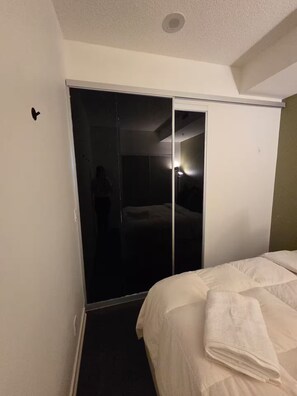 Hotellihuone, jossa on sänky, peilillä varustettu vaatekaappi ja ovi, joka johtaa pimeään huoneeseen.