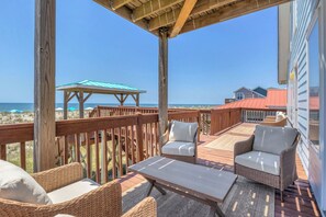 Eine Holzterrasse mit Korbmöbeln und einem Tisch, mit Blick auf Strand und Meer.
