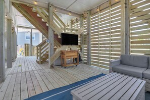 Eine Holzterrasse mit einer Couch und einem Fernseher, eine Treppe und ein Holzzaun.