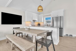 Une cuisine moderne avec des meubles blancs, un réfrigérateur en acier inoxydable et un coin repas comprenant une table et des chaises en bois.