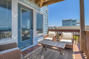 Une terrasse extérieure couverte, aménagée avec des meubles en osier, et une porte donnant accès à un bâtiment.
