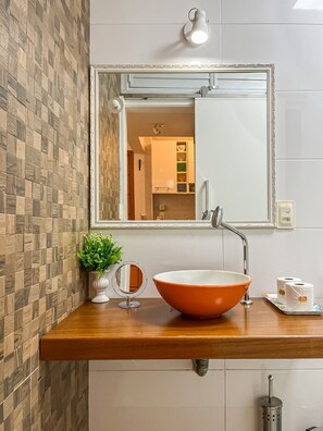Ein Badezimmer mit einem Holzwaschtisch, einem großen Spiegel, einem Topfspülbecken, einer kleinen Topfpflanze und einem Toilettenpapierhalter.