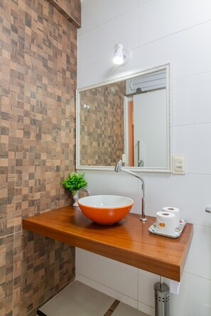Ein Badezimmer mit einem Holzbadezimmer-Möbel, einem großen Spiegel, einem Waschbecken mit orangenem Becken und einer kleinen Pflanze.