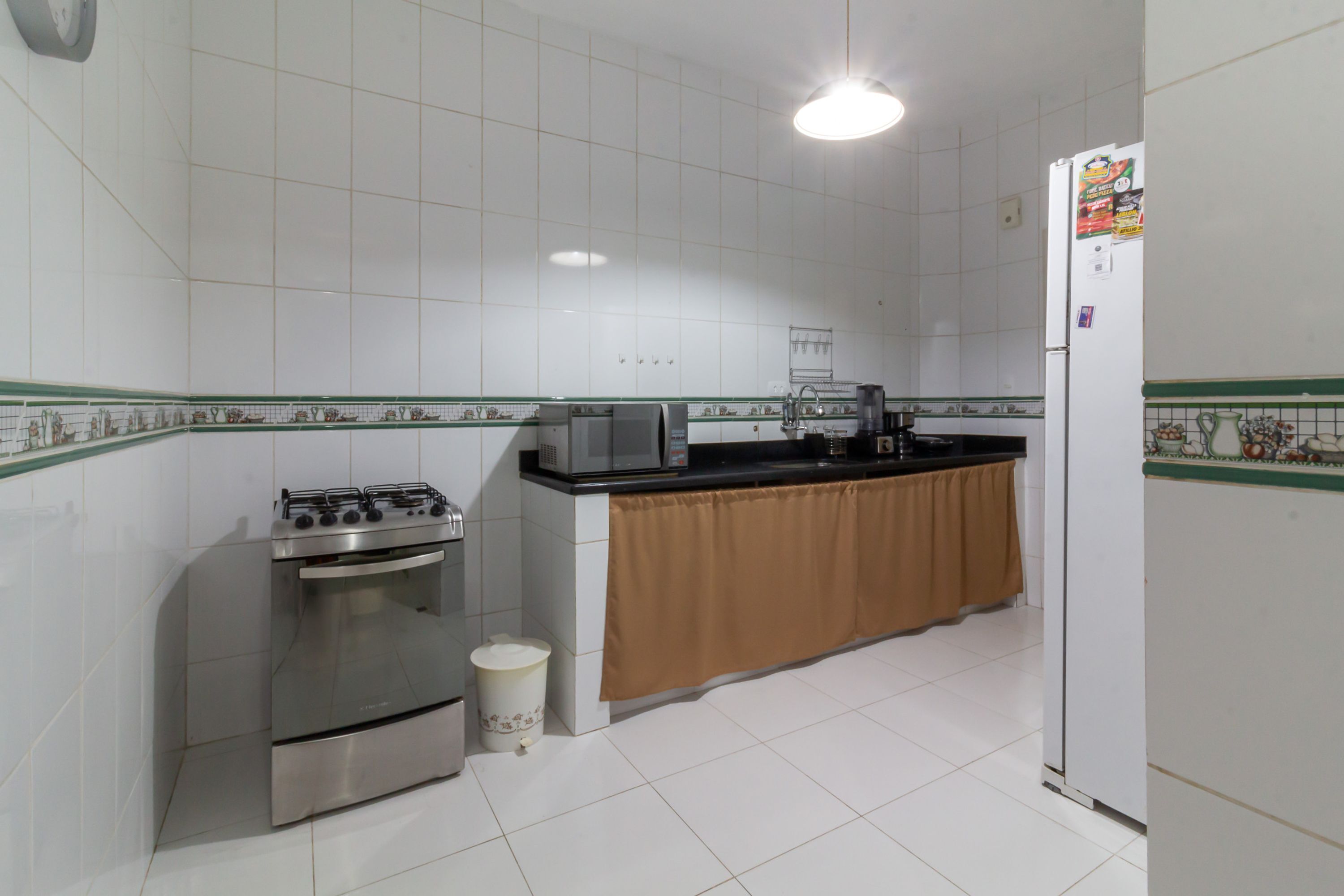 A kitchen with white tiled walls, a gas stove, an oven, a sink, and a refrigerator.