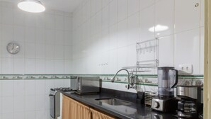 A kitchen with white tiles, a clock, a microwave, a coffee maker, and a sink. - 8 min da Praia de Ipanema Bt705 (Rio de Janeiro)