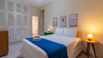 A bedroom with a bed, bedside tables, a wardrobe, and a door leading to another room.