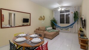 A dining area with a table set for four, a sofa, a hammock, and a television on the wall. - 8 min da Praia de Ipanema Bt705 (Rio de Janeiro)