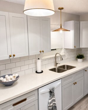 A modern kitchen with white cabinetry, a stainless steel sink, a bowl of eggs, and a hanging towel. - Remodeled Beachfront-Amazing Location! 
Gated Community. (Destin)
