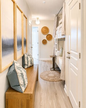 A hallway with a bench, a small table, and a bed with a canopy. There are wall-mounted baskets and a round woven rug on the floor. - Remodeled Beachfront-Amazing Location! 
Gated Community. (Destin)