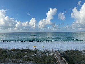 A beach with a wooden boardwalk leading to the shore, a sandy beach with umbrellas, and the ocean in the background. - Remodeled Beachfront-Amazing Location! 
Gated Community. (Destin)