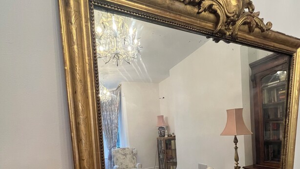 A room with a large ornate mirror, a chandelier, a floral armchair, a wooden cabinet, and a lamp. - Bluebell Suite at Elmwood House (Nottingham)