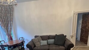 A living room with a dark brown sofa, patterned cushions, a dining table with chairs, and a chandelier. - Bluebell Suite at Elmwood House (Nottingham)