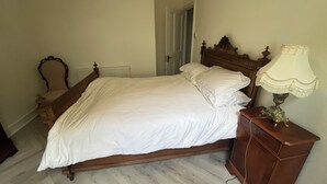A bedroom with a wooden bed, a nightstand with a lamp, and a door leading to another room. - Bluebell Suite at Elmwood House (Nottingham)