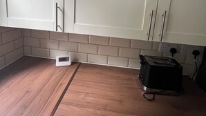 A kitchen with white cabinets, a wooden countertop, a digital clock, and a toaster. - Bluebell Suite at Elmwood House (Nottingham)