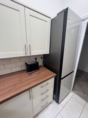 A kitchen with white cabinets, a black refrigerator, a wooden countertop, and a toaster. - Bluebell Suite at Elmwood House (Nottingham)