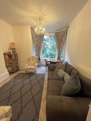 A living room with a brown sofa, patterned armchair, and a chandelier. - Bluebell Suite at Elmwood House (Nottingham)