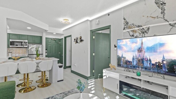 Ein modernes Wohnzimmer mit Flachbildfernseher, einem Essbereich mit weißen Stühlen und einer Küche mit grünen Schränken.