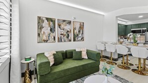 Ein modernes Wohnzimmer mit einem grünen Sofa, einem weißen Esstisch und abstrakter Kunst an der Wand.