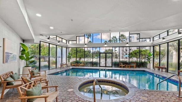 Ein moderner Poolbereich im Innenbereich mit Whirlpool, Liegestühlen und Blick auf die Stadt.