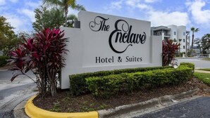 Ein Schild für The Enclave Hotel & Suites mit modernem Design, das eine große, gut lesbare Schriftart und gepflegte Bepflanzung zeigt.