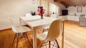 A dining area with a white table and chairs, a vase of flowers, and a wooden ceiling. - Altana 9001 • Designer Attic with a View of the City Walls and an Elevator (Lucca)