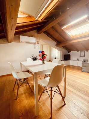 Ein Essbereich mit einem weißen Tisch und Stühlen, einer Blumenvase und einer Holzbalkendecke.