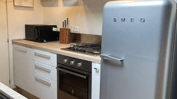 Eine Küche mit einem Edelstahl-Kühlschrank, Backofen und einer Mikrowelle. Es sind Schränke, ein Spülbecken und eine Arbeitsplatte vorhanden.
