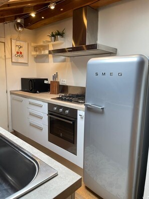 Eine Küche mit einem Edelstahl-Kühlschrank, Backofen und einer Mikrowelle. Es sind Schränke, ein Spülbecken und eine Arbeitsplatte vorhanden.