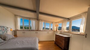 Un dormitorio con cama, cómoda de madera y varias ventanas con cortinas.